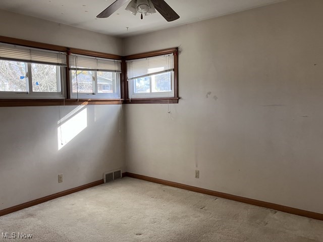 carpeted spare room featuring ceiling fan and plenty of natural light