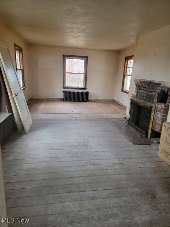 unfurnished living room with radiator, light hardwood / wood-style flooring, and a brick fireplace