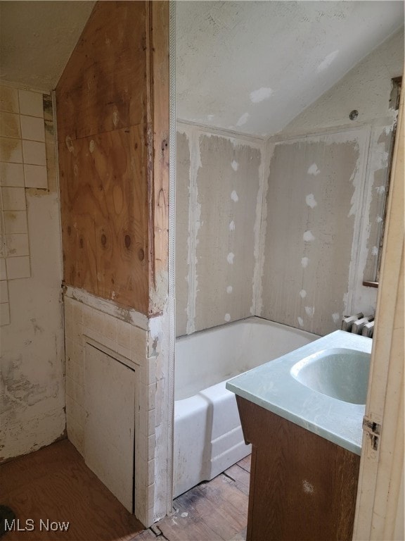 bathroom featuring a washtub, vanity, hardwood / wood-style flooring, and vaulted ceiling