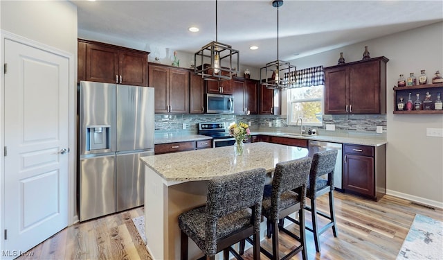 kitchen featuring stainless steel appliances, sink, decorative light fixtures, a center island, and light hardwood / wood-style floors