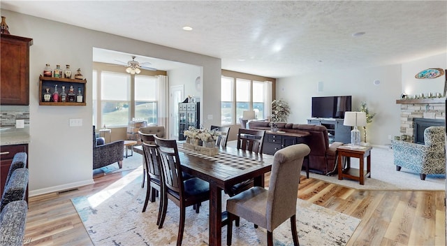 dining area featuring a fireplace, a textured ceiling, light hardwood / wood-style floors, and ceiling fan