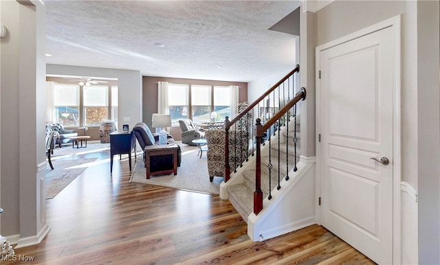 stairs with ceiling fan, wood-type flooring, and a textured ceiling