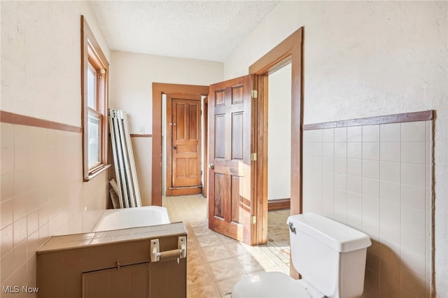 bathroom featuring vanity, a textured ceiling, toilet, and tile walls