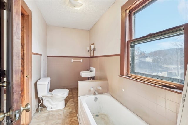 bathroom featuring a textured ceiling, a tub to relax in, toilet, and tile walls