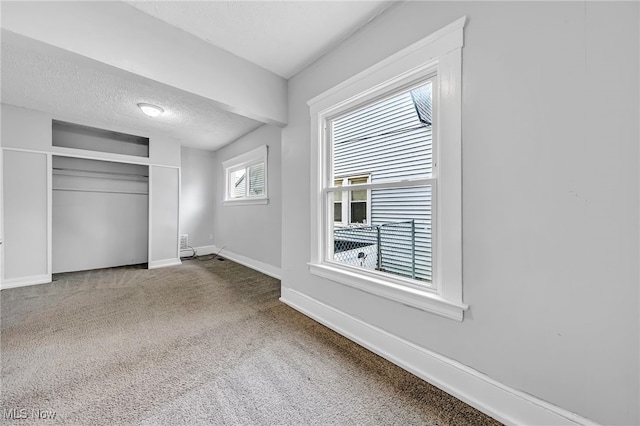 unfurnished bedroom with baseboards, carpet flooring, a textured ceiling, and a closet