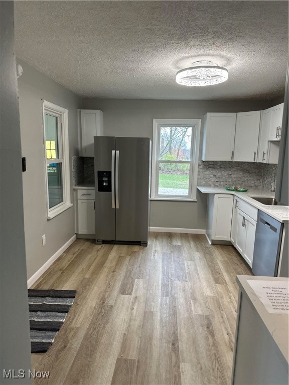 kitchen with white cabinets, sink, light hardwood / wood-style flooring, appliances with stainless steel finishes, and tasteful backsplash