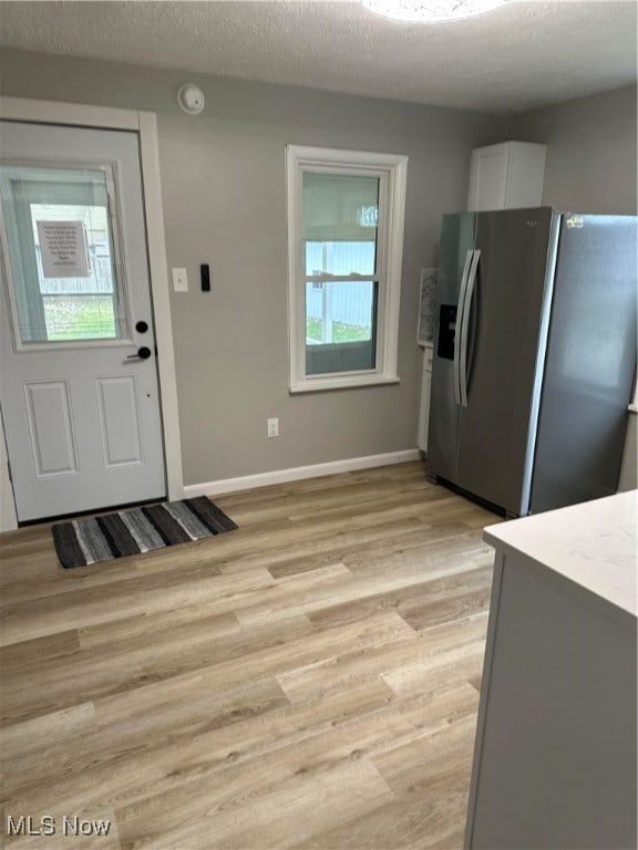 kitchen featuring white cabinetry, stainless steel fridge with ice dispenser, light hardwood / wood-style floors, and a textured ceiling