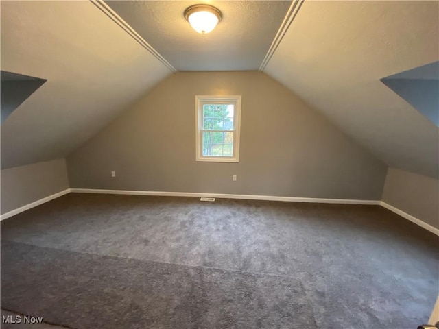 bonus room with a textured ceiling, vaulted ceiling, and dark colored carpet