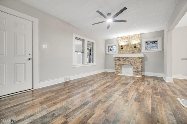 unfurnished living room with hardwood / wood-style flooring, ceiling fan, a stone fireplace, and a textured ceiling