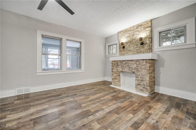 unfurnished living room with a textured ceiling, ceiling fan, a stone fireplace, and dark wood-type flooring