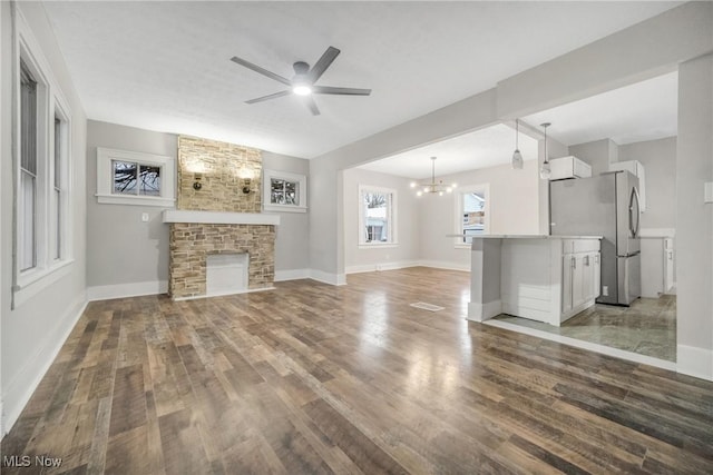 unfurnished living room with a stone fireplace, dark hardwood / wood-style flooring, and ceiling fan with notable chandelier