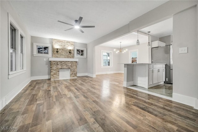 unfurnished living room featuring a fireplace, ceiling fan with notable chandelier, and hardwood / wood-style flooring