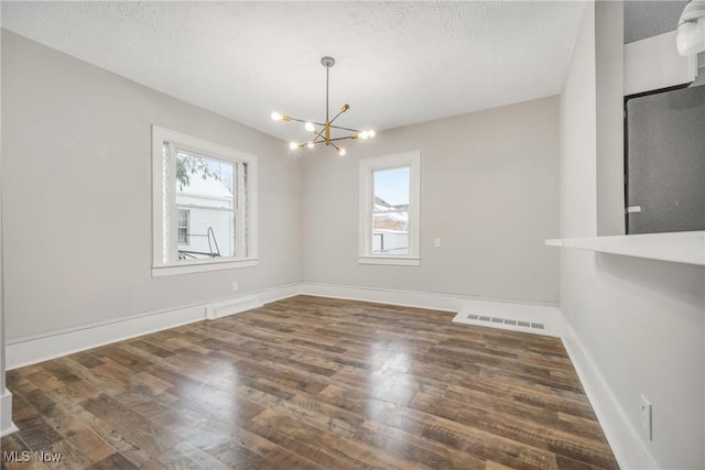 unfurnished dining area featuring dark wood-type flooring, a chandelier, and a textured ceiling