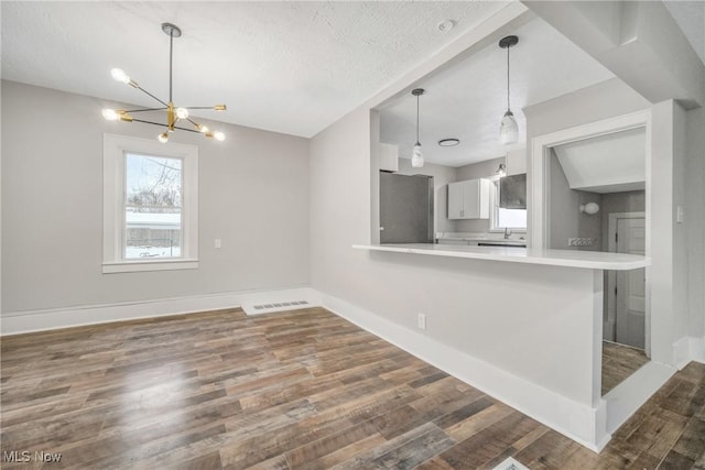 kitchen featuring kitchen peninsula, dark hardwood / wood-style flooring, a textured ceiling, an inviting chandelier, and stainless steel refrigerator