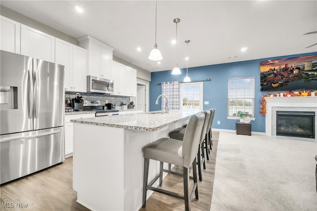 kitchen with pendant lighting, light hardwood / wood-style floors, stainless steel appliances, and a kitchen island with sink