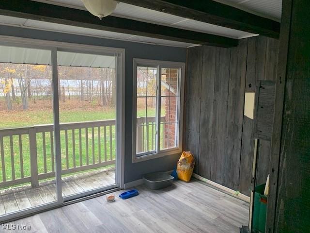 doorway with beam ceiling, wooden walls, and wood-type flooring