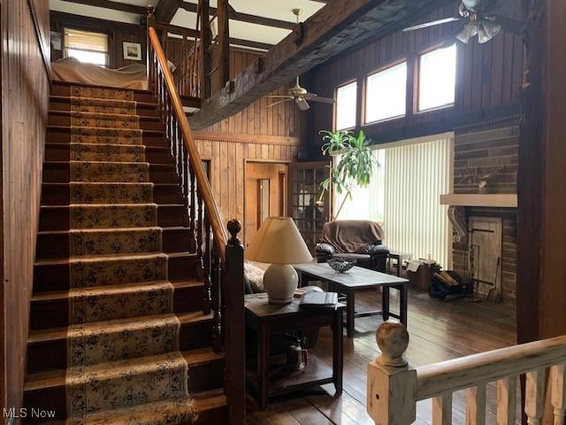 living room with hardwood / wood-style floors, beam ceiling, ceiling fan, and wooden walls