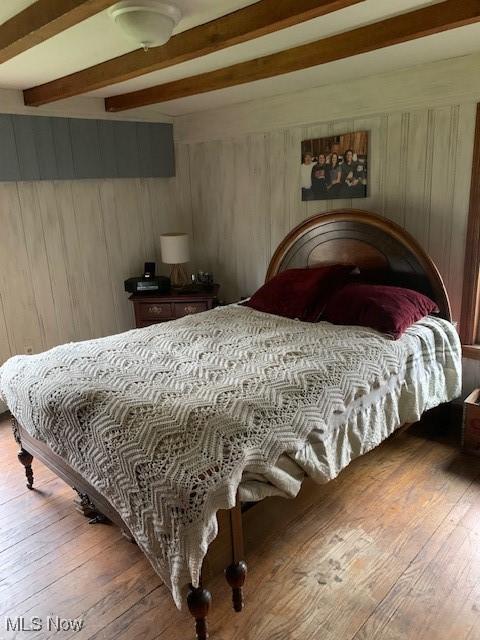 bedroom with wood-type flooring, wooden walls, and beam ceiling