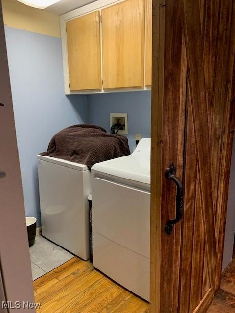 washroom with washing machine and clothes dryer, light hardwood / wood-style floors, and cabinets