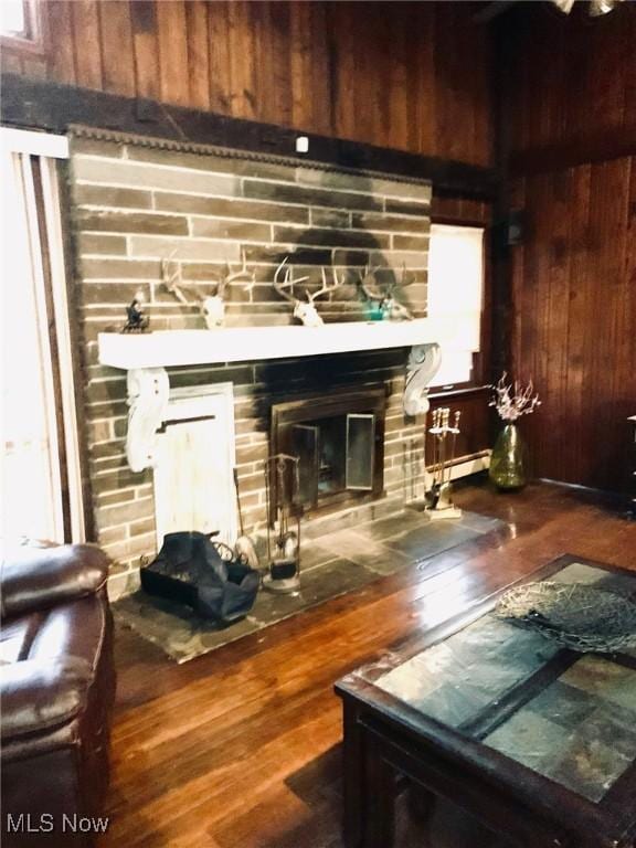 living room featuring a baseboard heating unit, a stone fireplace, wood walls, and hardwood / wood-style flooring