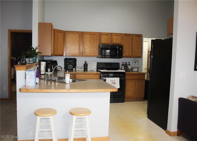 kitchen featuring sink, kitchen peninsula, a towering ceiling, a kitchen bar, and black appliances