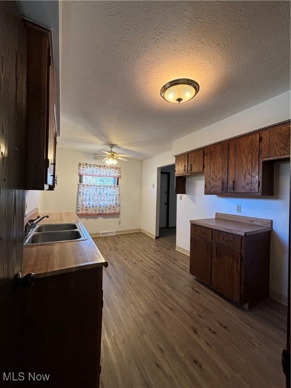 kitchen featuring dark wood-type flooring, sink, ceiling fan, a textured ceiling, and dark brown cabinets