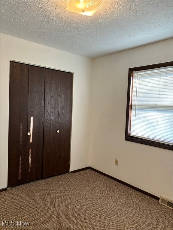 unfurnished bedroom featuring light carpet, a textured ceiling, and a closet