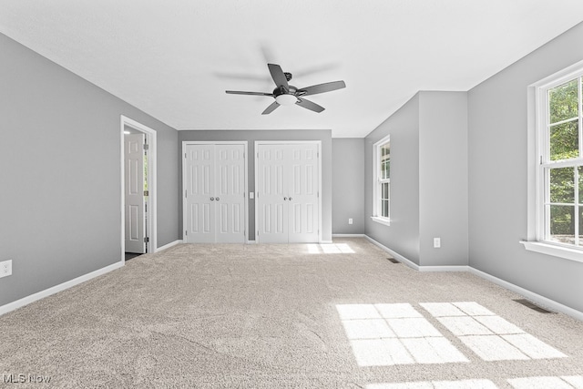 unfurnished bedroom with two closets, light colored carpet, and ceiling fan