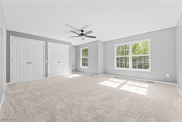 unfurnished bedroom with a textured ceiling, carpet floors, ceiling fan, and multiple closets