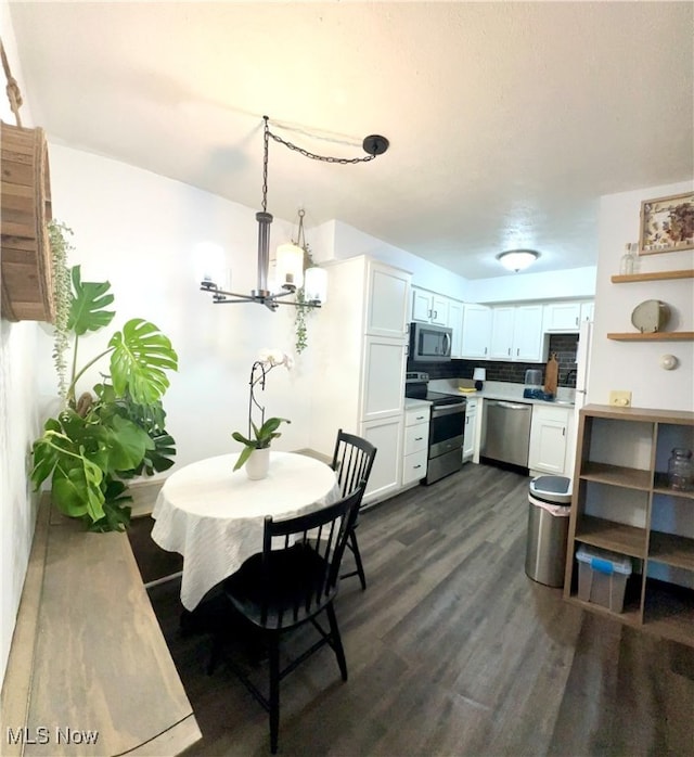 kitchen featuring dark wood-type flooring, white cabinets, decorative backsplash, appliances with stainless steel finishes, and decorative light fixtures