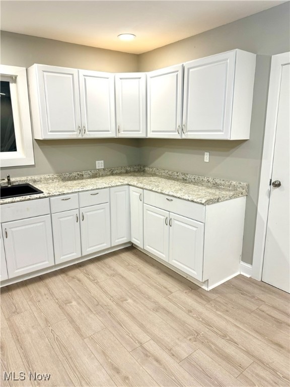 kitchen featuring light hardwood / wood-style floors, light stone counters, white cabinetry, and sink