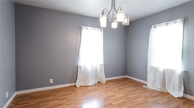 unfurnished room with plenty of natural light, a chandelier, and light hardwood / wood-style flooring