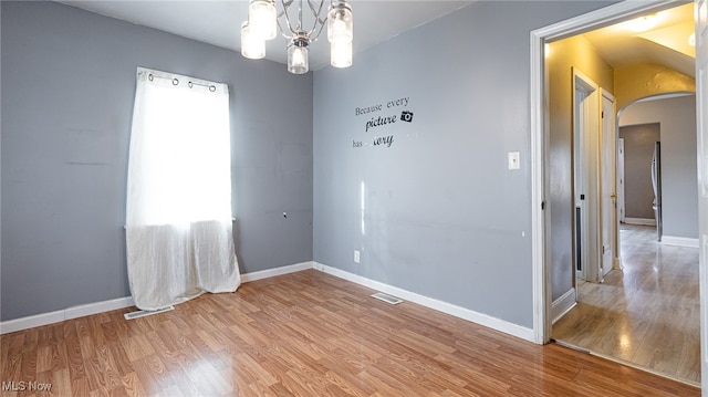 empty room with wood-type flooring and an inviting chandelier