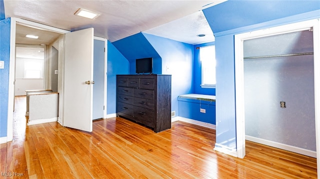 unfurnished bedroom with multiple windows, a closet, hardwood / wood-style floors, and lofted ceiling