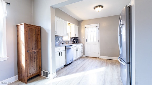 kitchen featuring sink, tasteful backsplash, light hardwood / wood-style floors, white cabinets, and appliances with stainless steel finishes