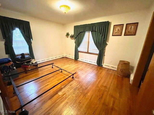 exercise room featuring wood-type flooring and a baseboard heating unit