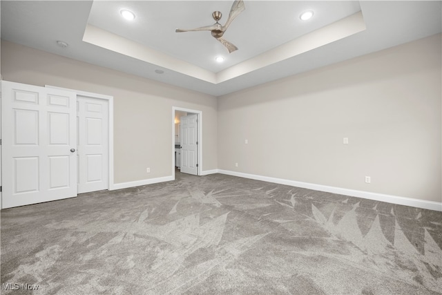 unfurnished bedroom with a tray ceiling, a closet, ceiling fan, and carpet flooring