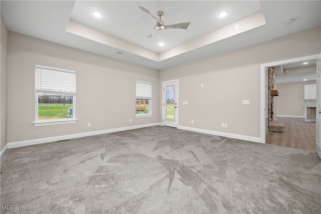 empty room with carpet flooring, a raised ceiling, and ceiling fan