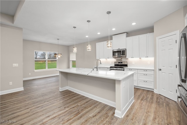 kitchen featuring a kitchen island with sink, white cabinets, hanging light fixtures, light hardwood / wood-style flooring, and stainless steel appliances