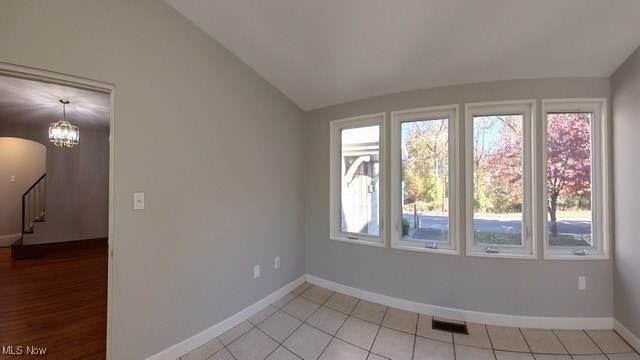 unfurnished room with vaulted ceiling, a wealth of natural light, a notable chandelier, and light tile patterned flooring