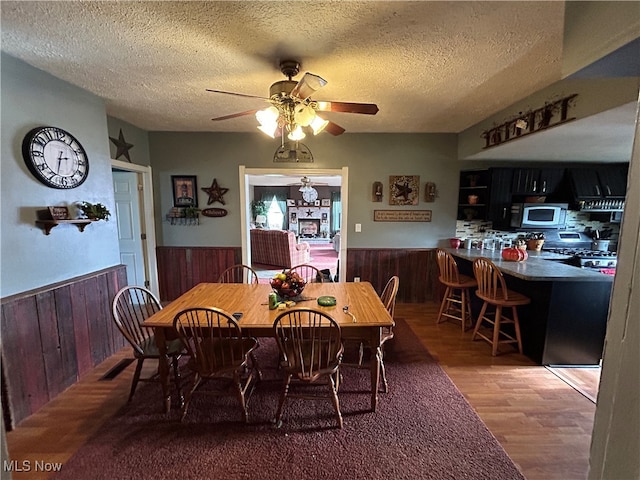 dining space featuring ceiling fan with notable chandelier, wood-type flooring, a textured ceiling, and wooden walls