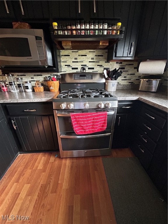 kitchen with ventilation hood, stainless steel appliances, tasteful backsplash, and light hardwood / wood-style floors