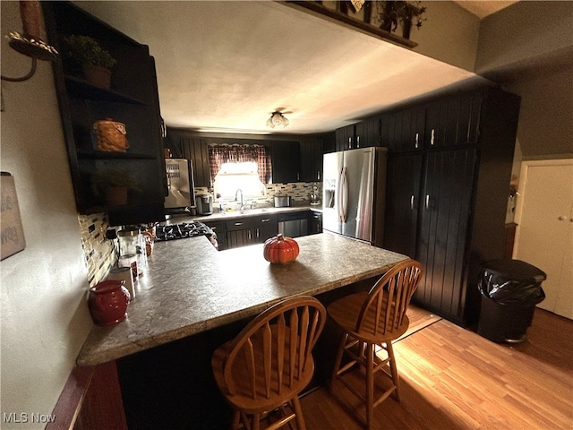 kitchen featuring sink, stainless steel refrigerator with ice dispenser, light hardwood / wood-style floors, kitchen peninsula, and a breakfast bar area