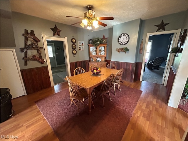 dining space featuring a textured ceiling, hardwood / wood-style flooring, ceiling fan, and wood walls