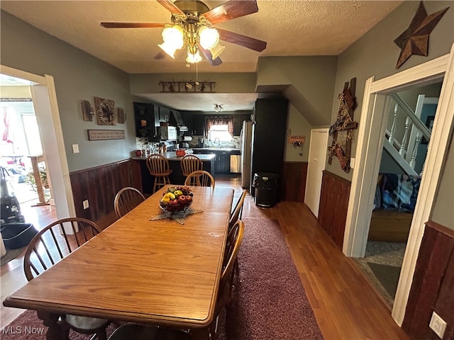 dining space with ceiling fan, hardwood / wood-style floors, wood walls, and a textured ceiling