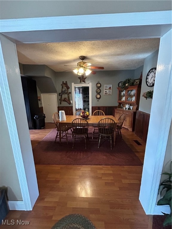 dining area with ceiling fan, dark hardwood / wood-style flooring, a textured ceiling, and wooden walls