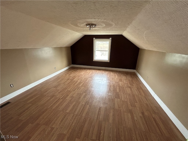 additional living space with a textured ceiling, hardwood / wood-style flooring, and lofted ceiling