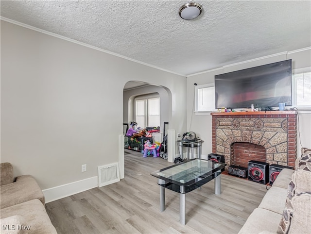 living room featuring crown molding, a fireplace, a textured ceiling, and light wood-type flooring