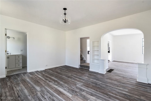 empty room featuring dark hardwood / wood-style flooring, built in features, and a notable chandelier