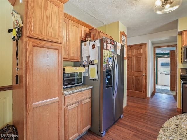 kitchen with light stone counters, a textured ceiling, stainless steel appliances, dark wood-type flooring, and light brown cabinets